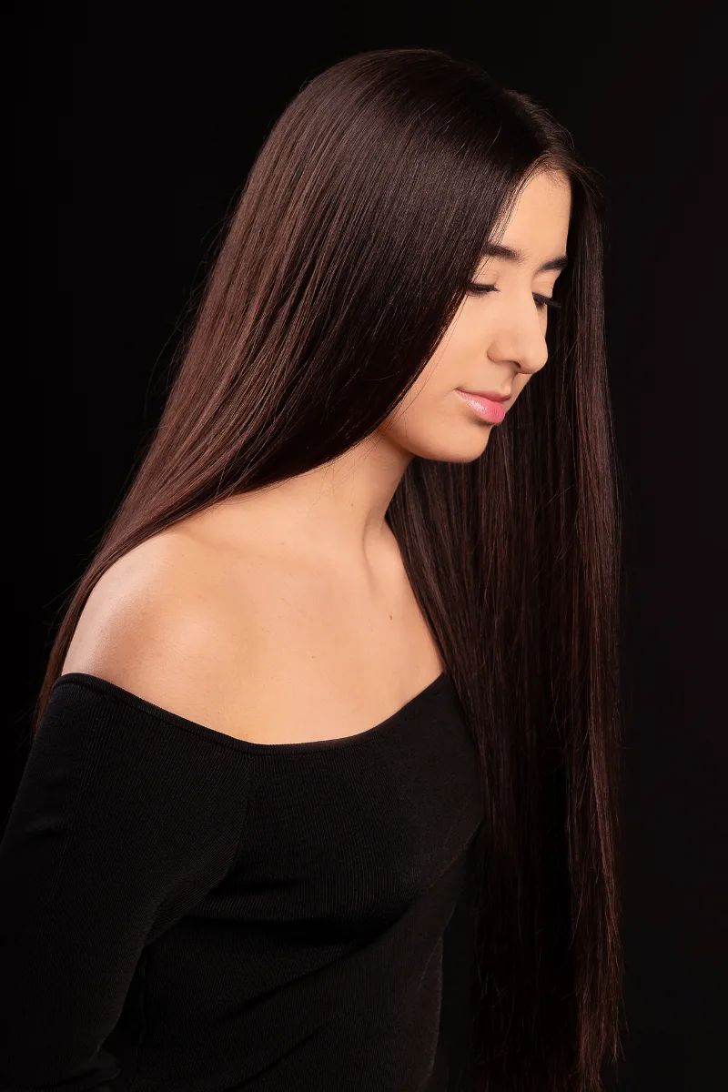Beauty-Portrait einer jungen Frau im Profil, langes glattes braunes Haar, schwarzer Studio-Hintergrund
