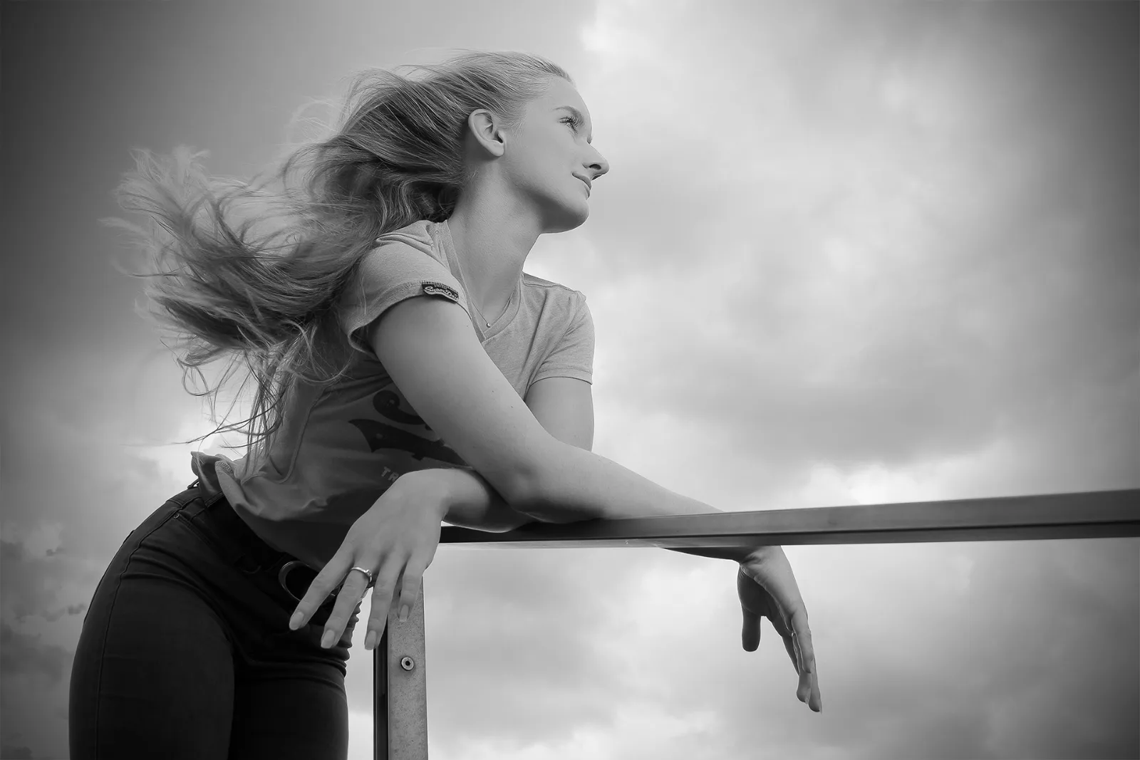 Beauty-Portrait einer jungen Frau in Schwarz-Weiß, das Haar weht im Wind, im Hintergrund ein wolkenverhangener Himmel