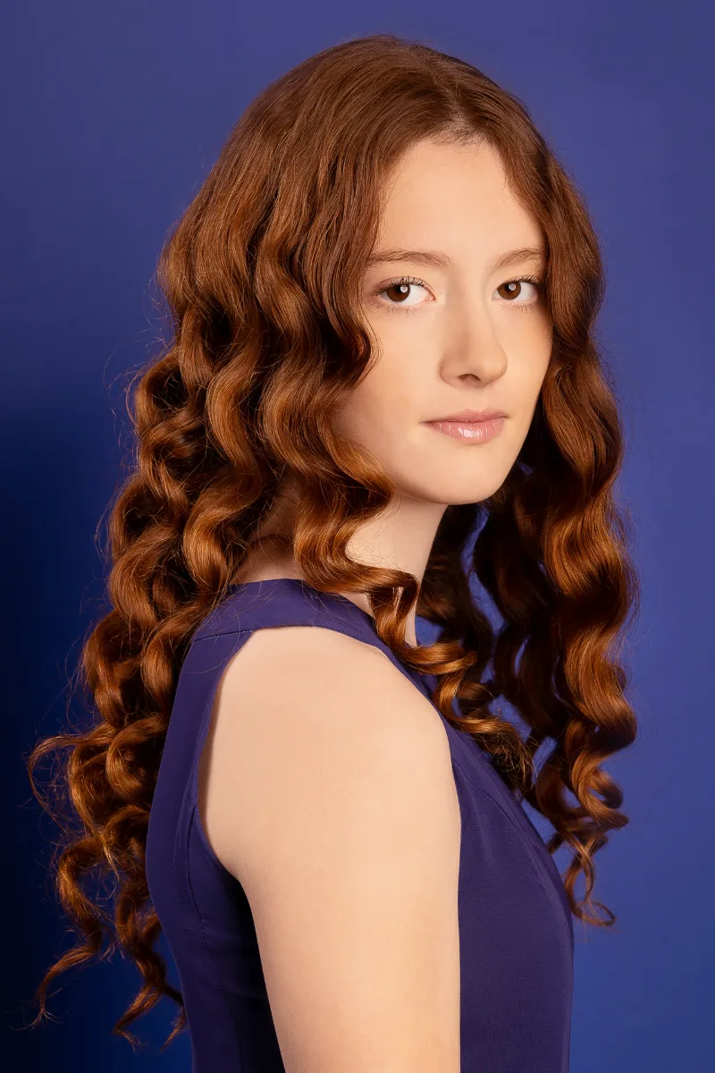 Beauty-Portrait eines Mädchens mit langen roten Locken, blauer Studio-Hintergrund, blaues Kleid