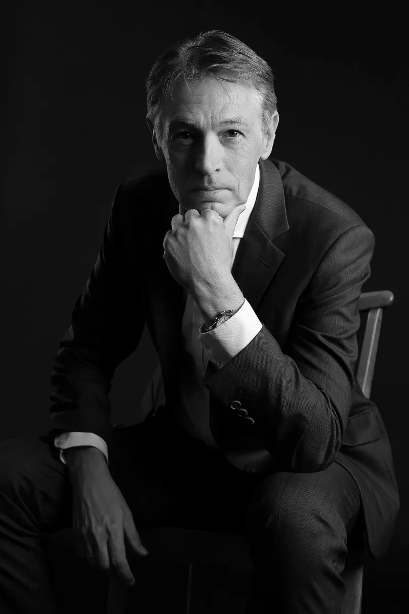 Schwarz-Weiß-Studio-Portrait: Mann im Anzug auf einem Stuhl, Hand am Kinn, dunkler Hintergrund