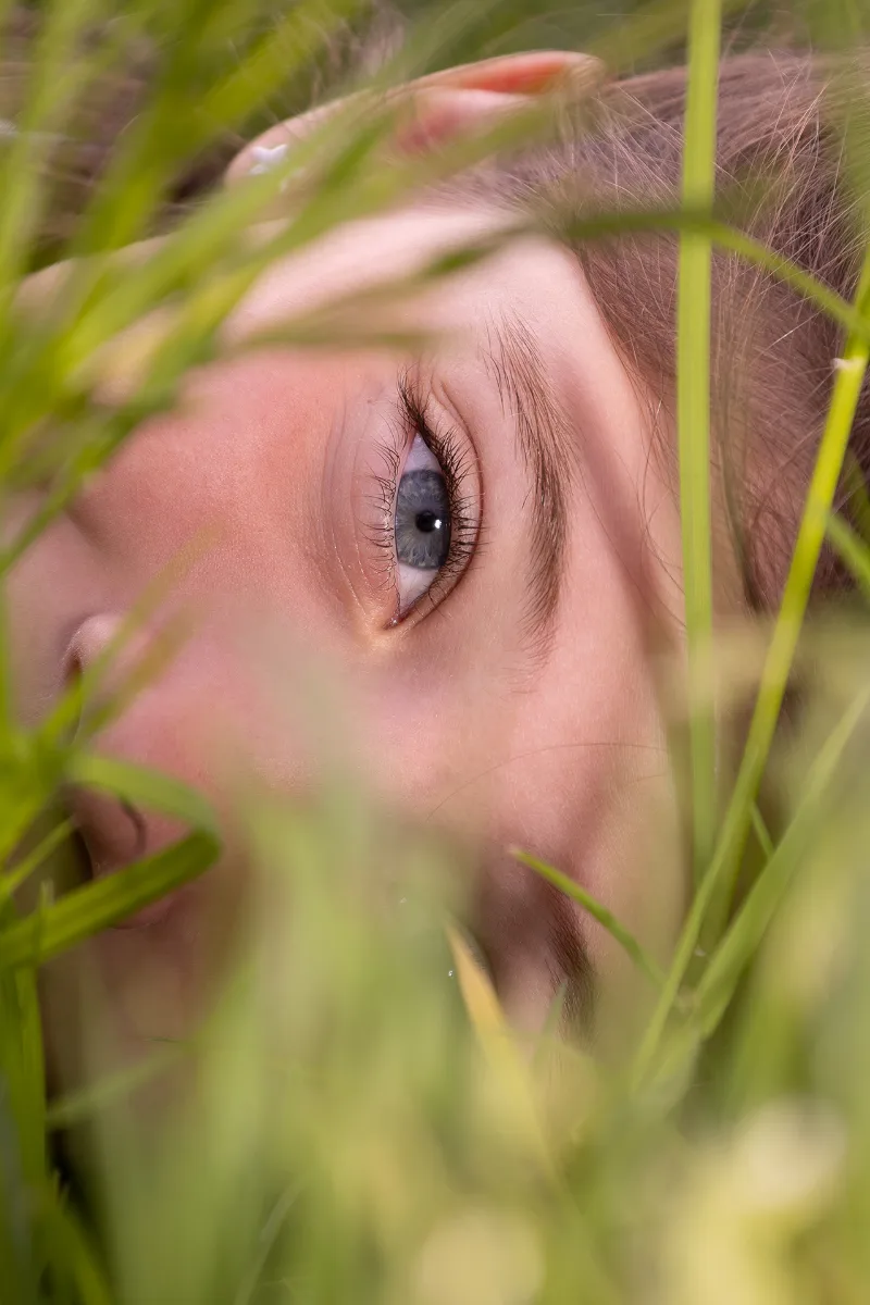 Nahaufnahme eines im Wiesengras liegenden Kindergesichts, ein blaues Auge in scharfem Fokus