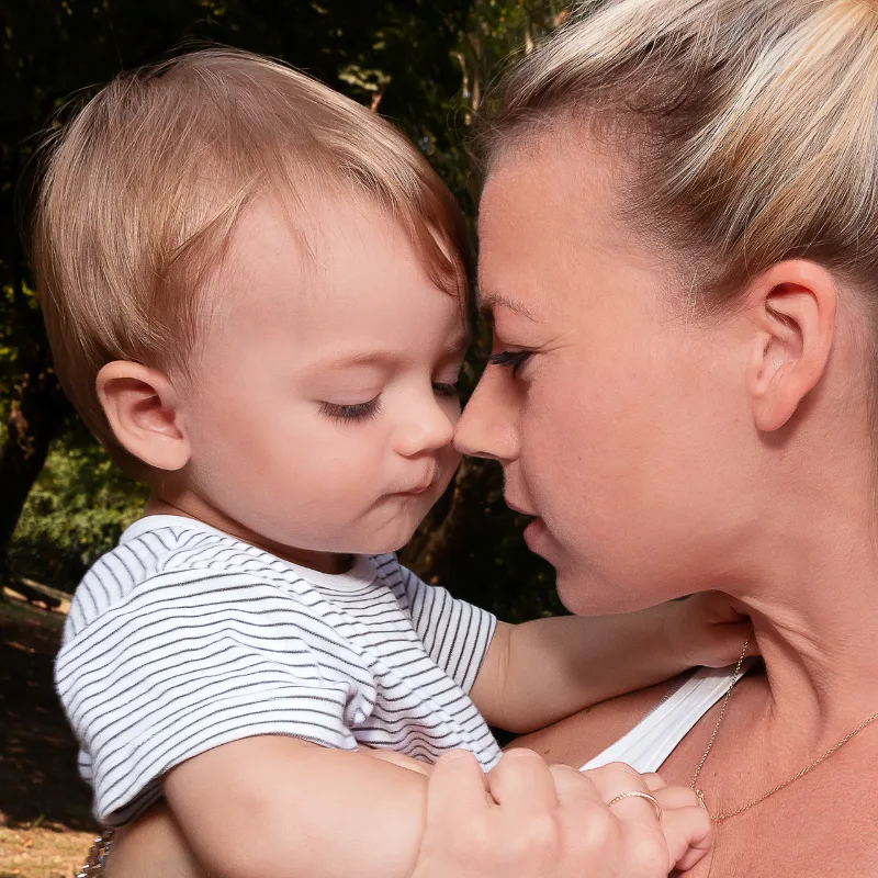 Blonder Kleinkindjunge und seine Mutter Stirn an Stirn im warmen Gegenlicht