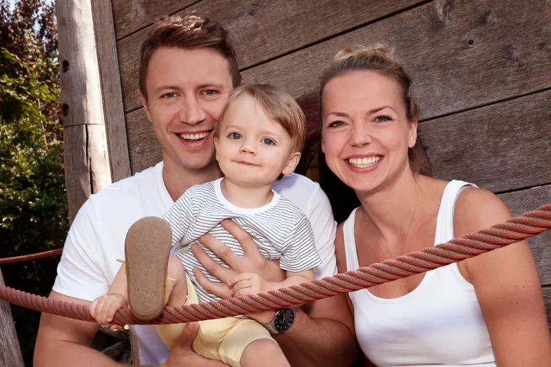 Junge Familie mit Kleinkind an einem Holz-Spielgerät im warmen Abendlicht